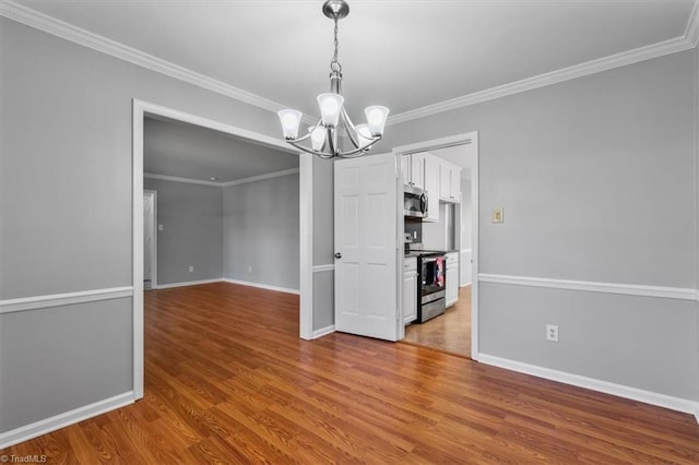 unfurnished dining area featuring baseboards, a notable chandelier, wood finished floors, and crown molding