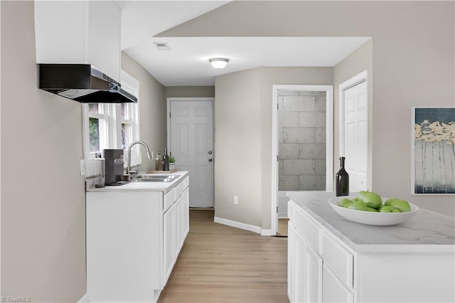 kitchen with white cabinets, wall chimney range hood, sink, light hardwood / wood-style floors, and light stone counters