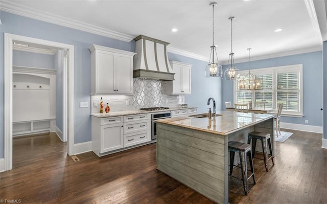 kitchen with stainless steel oven, white cabinets, an island with sink, and decorative light fixtures