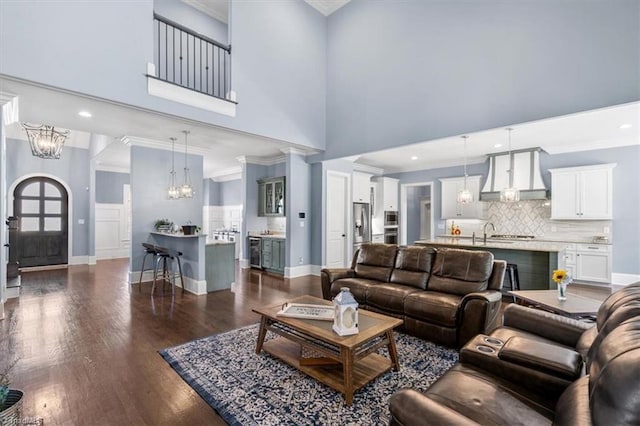 living room featuring a towering ceiling, dark hardwood / wood-style floors, ornamental molding, and a notable chandelier