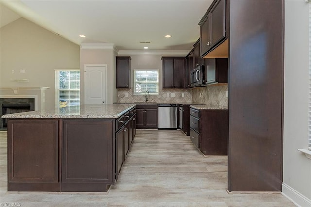 kitchen with dark brown cabinetry, light stone counters, appliances with stainless steel finishes, a kitchen island, and backsplash