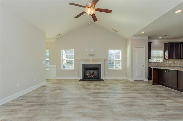 unfurnished living room featuring a fireplace, sink, light hardwood / wood-style flooring, and a wealth of natural light