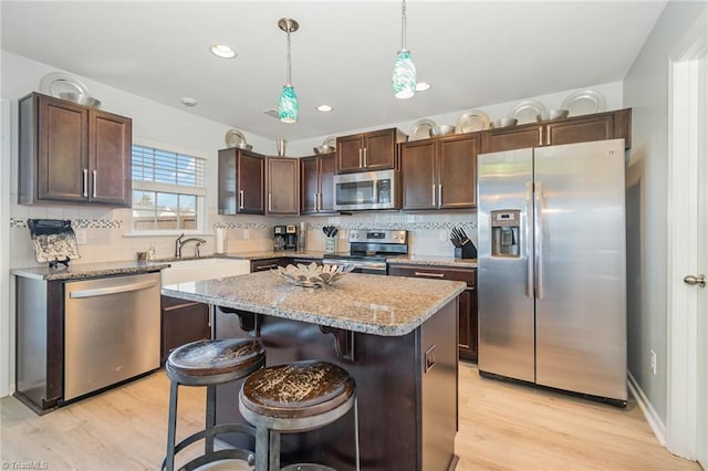 kitchen with dark brown cabinets, backsplash, decorative light fixtures, stainless steel appliances, and a sink