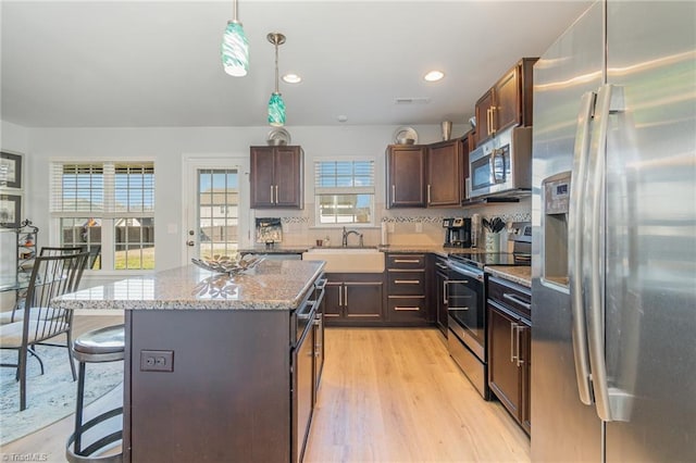 kitchen with a breakfast bar, a sink, stainless steel appliances, light wood-style floors, and dark brown cabinets