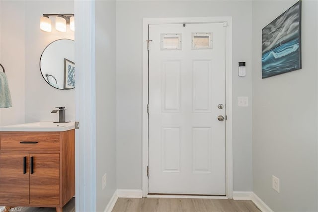 doorway with a sink, baseboards, and light wood finished floors