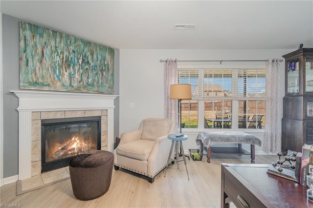 living area featuring a tiled fireplace, wood finished floors, and visible vents