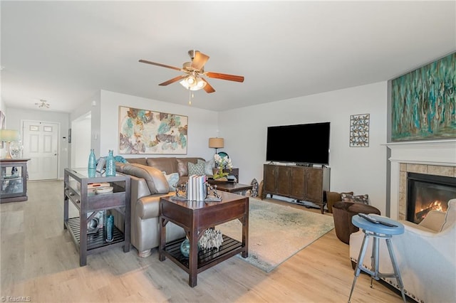 living room with light wood-style floors, ceiling fan, and a tiled fireplace