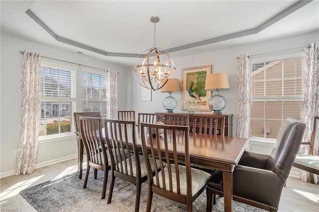 dining area with a raised ceiling, a notable chandelier, wood finished floors, and baseboards