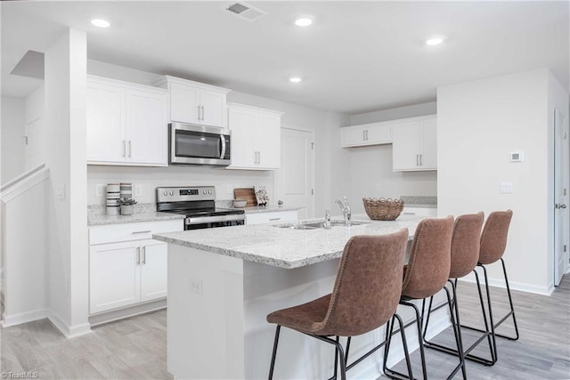 kitchen with sink, stainless steel appliances, light hardwood / wood-style floors, white cabinets, and a center island with sink