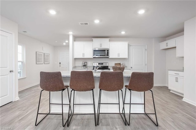 kitchen with white cabinetry, light stone countertops, stainless steel appliances, and a center island with sink