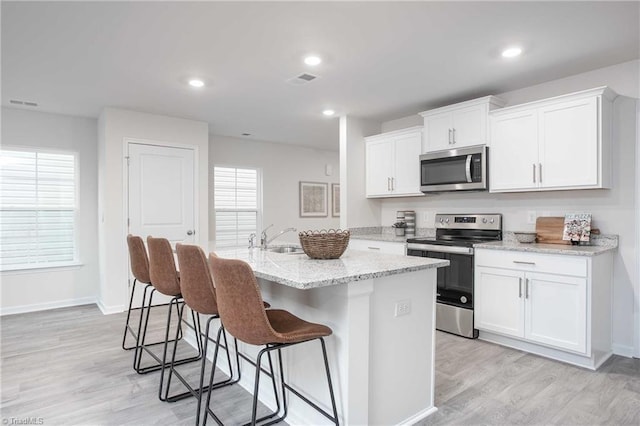 kitchen with sink, light stone counters, a center island with sink, appliances with stainless steel finishes, and white cabinets