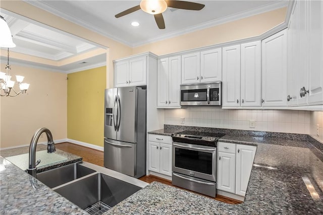 kitchen with hanging light fixtures, stainless steel appliances, decorative backsplash, ceiling fan with notable chandelier, and white cabinets