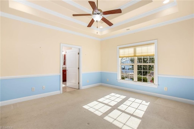 empty room with a raised ceiling, ceiling fan, ornamental molding, and light carpet