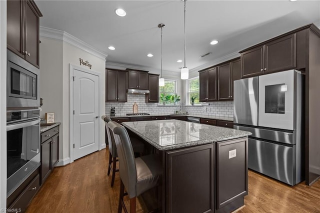 2590 Mccullum Ct, Browns Summit, NC 27214 - kitchen with stainless steel appliances, dark brown cabinetry, decorative backsplash, a center island, and light stone counters