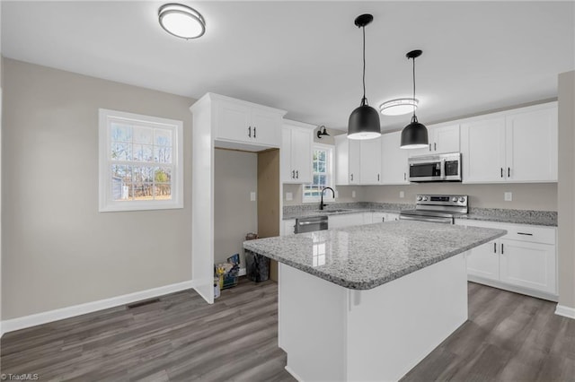 kitchen featuring white cabinetry, appliances with stainless steel finishes, decorative light fixtures, a kitchen island, and light stone counters