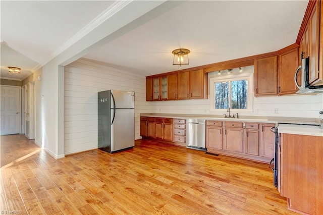 kitchen with appliances with stainless steel finishes, crown molding, sink, light hardwood / wood-style flooring, and wood walls