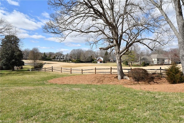 view of property's community featuring a rural view, a lawn, and fence