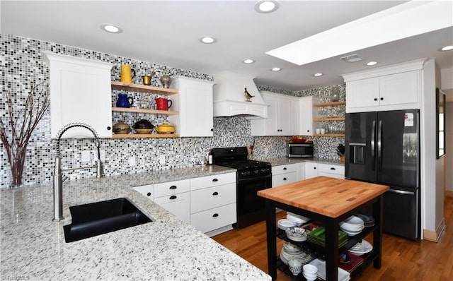 kitchen with light stone countertops, open shelves, a skylight, a sink, and black appliances