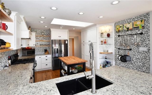 kitchen with light stone counters, open shelves, a sink, black appliances, and white cabinets