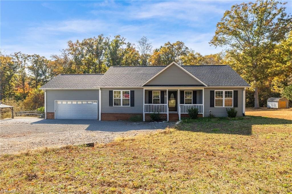 ranch-style house featuring a front lawn, a shed, a garage, and covered porch