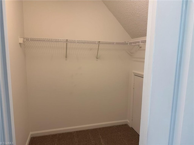 spacious closet featuring lofted ceiling and dark colored carpet