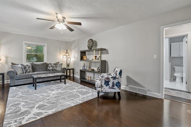 living room featuring dark wood-type flooring, ceiling fan, and a textured ceiling