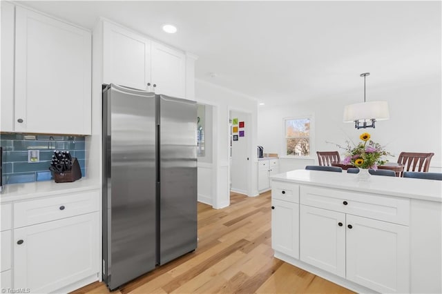 kitchen with light wood-type flooring, white cabinetry, stainless steel fridge, and hanging light fixtures