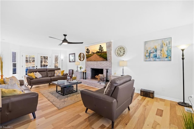 living room with ceiling fan, light hardwood / wood-style flooring, a brick fireplace, and french doors