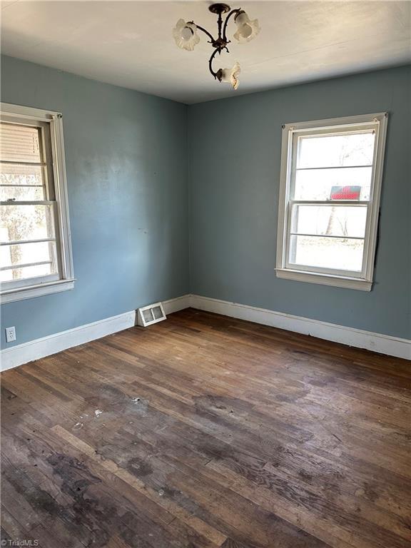 unfurnished room featuring dark wood-style floors, visible vents, and baseboards