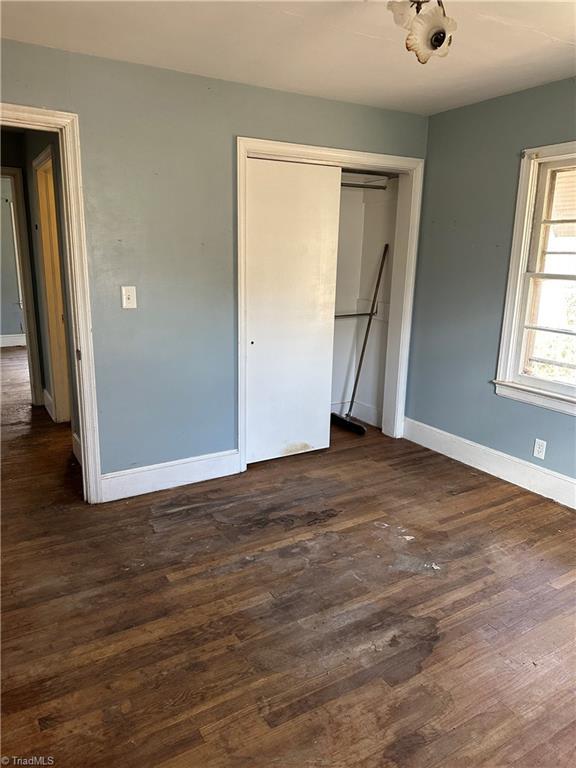 unfurnished bedroom featuring dark wood-style floors, a closet, and baseboards