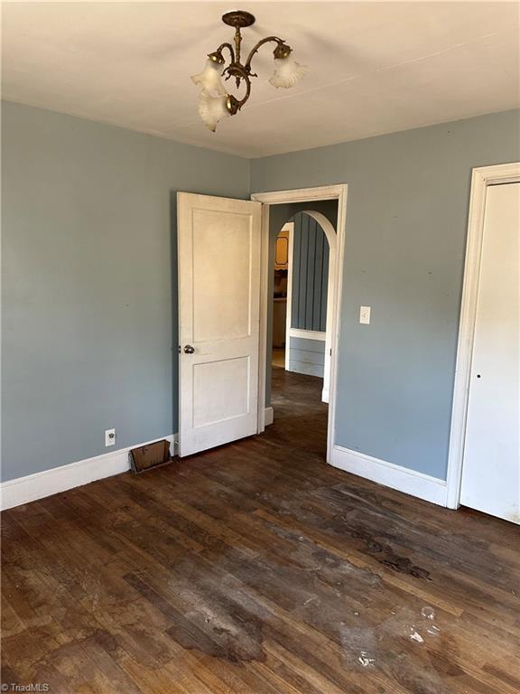 spare room featuring a chandelier, arched walkways, dark wood finished floors, and baseboards