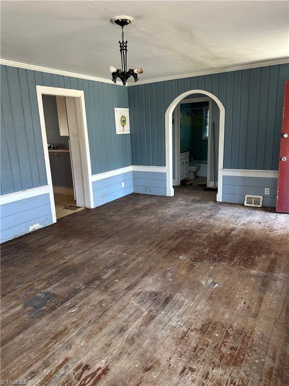 unfurnished dining area with arched walkways, visible vents, ornamental molding, a chandelier, and hardwood / wood-style floors