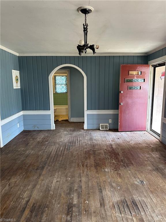 unfurnished dining area featuring a healthy amount of sunlight, wood-type flooring, visible vents, and arched walkways