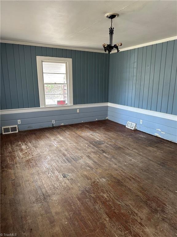 empty room featuring a chandelier, visible vents, crown molding, and hardwood / wood-style flooring