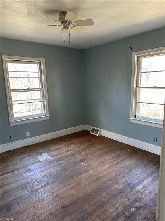 empty room with dark wood-style floors, visible vents, baseboards, and a ceiling fan