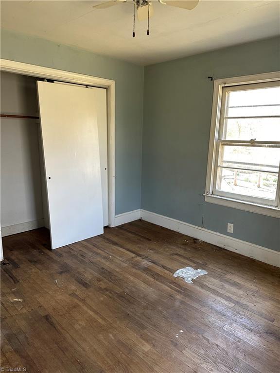 unfurnished bedroom featuring a ceiling fan, a closet, baseboards, and dark wood-style flooring