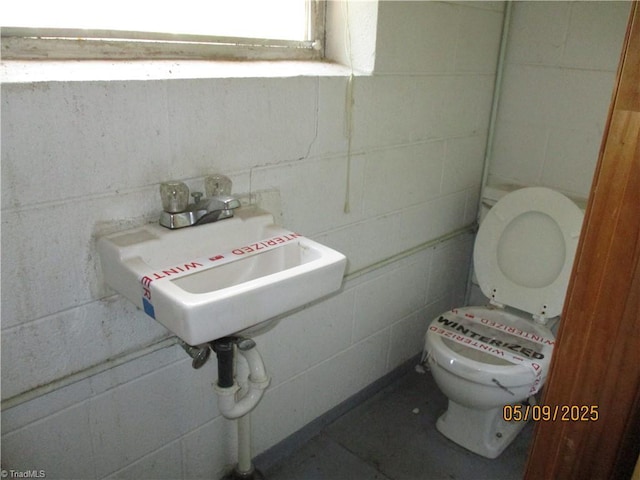 bathroom with toilet, a sink, and concrete block wall