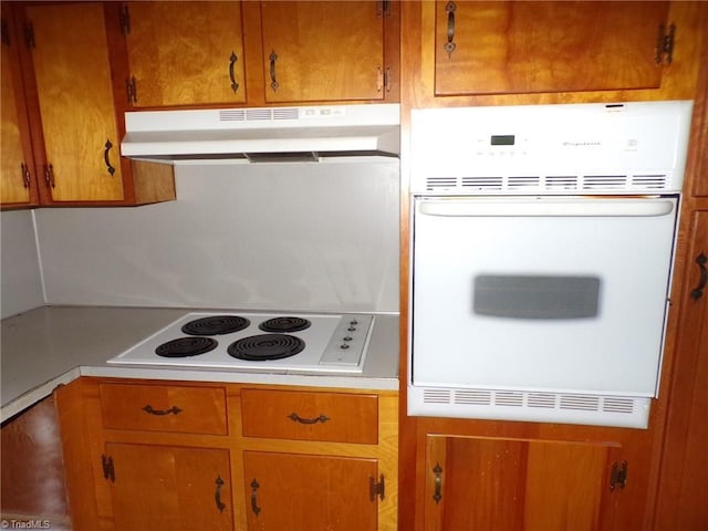 kitchen featuring white appliances, under cabinet range hood, brown cabinetry, and light countertops
