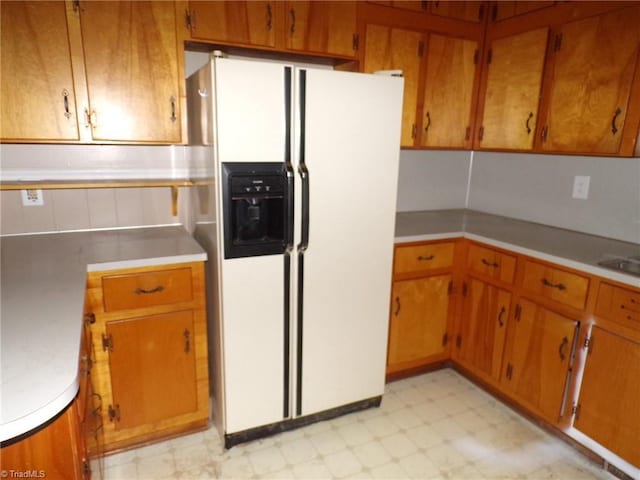 kitchen with white refrigerator with ice dispenser, light floors, brown cabinets, and light countertops