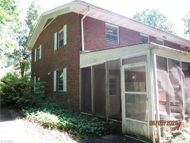 view of property exterior featuring brick siding and a sunroom