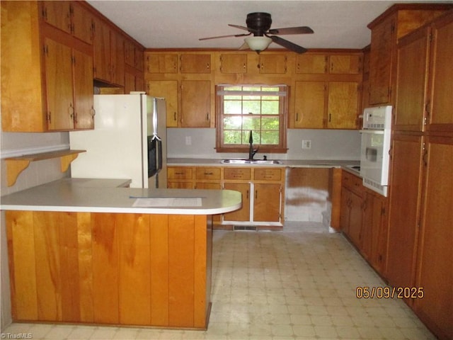 kitchen with a sink, white appliances, light floors, a ceiling fan, and a peninsula
