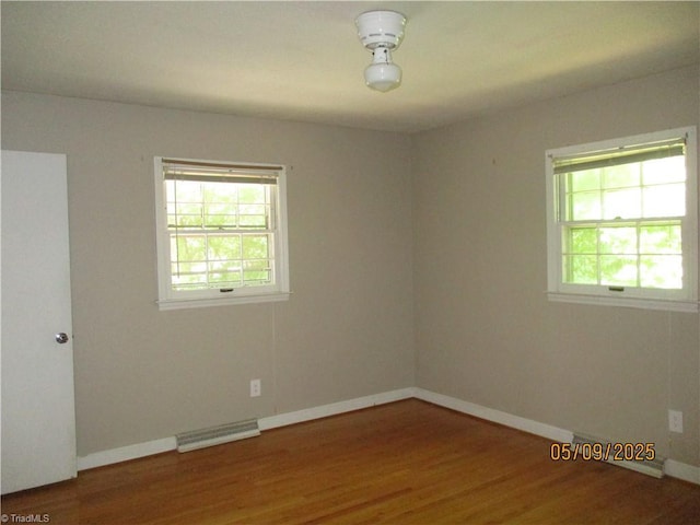 empty room featuring plenty of natural light, wood finished floors, and baseboards