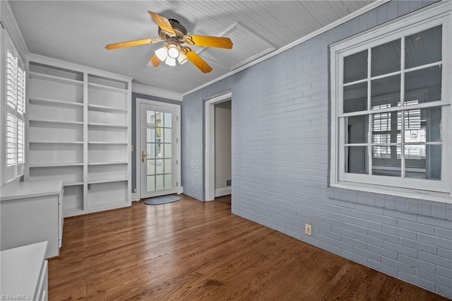 unfurnished living room with crown molding, ceiling fan, hardwood / wood-style floors, and brick wall