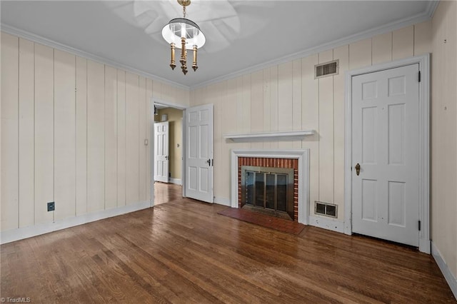 unfurnished living room featuring ornamental molding, dark hardwood / wood-style floors, a brick fireplace, and a notable chandelier