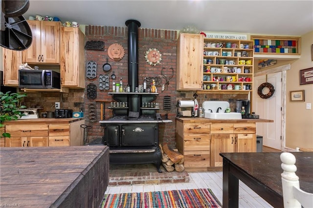 kitchen featuring a wood stove, light hardwood / wood-style flooring, butcher block counters, brick wall, and light brown cabinetry