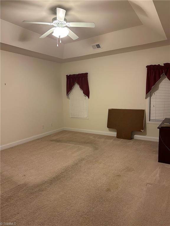 carpeted spare room featuring a tray ceiling and ceiling fan