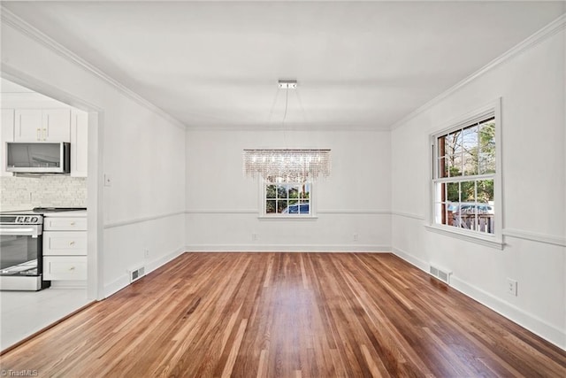 unfurnished dining area featuring wood-type flooring, ornamental molding, and an inviting chandelier