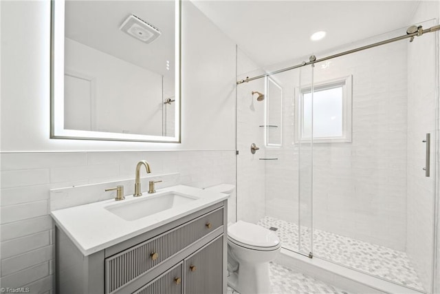 bathroom with walk in shower, vanity, tile walls, and toilet