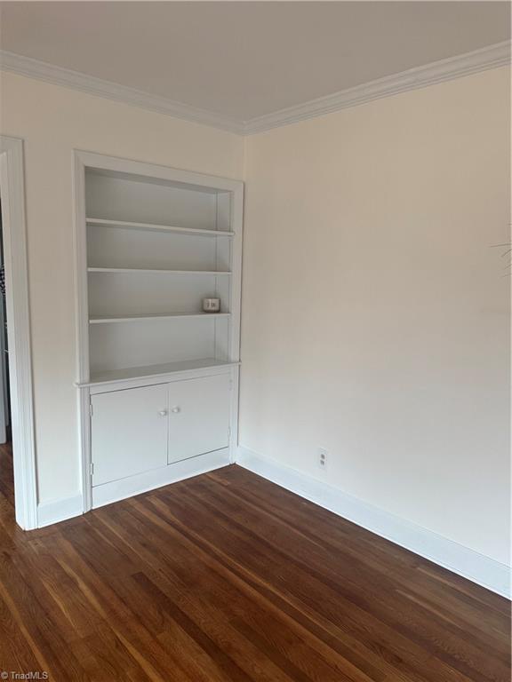 spare room with built in shelves, dark hardwood / wood-style flooring, and ornamental molding