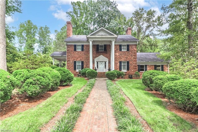 greek revival inspired property featuring a chimney, a front lawn, and brick siding